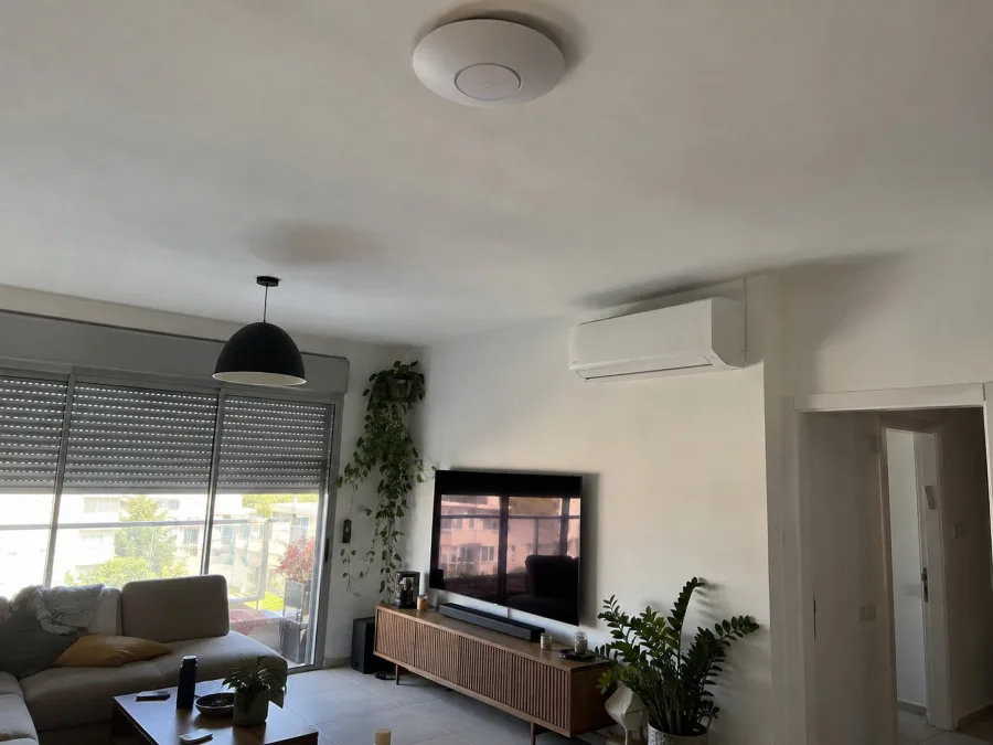נקודת גישה אלחוטית לבנה ועגולה על תקרה לבנה של סלון פתוח ומואר